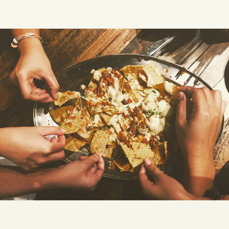 A shared plate of loaded nachos with melted cheese, being picked apart by hand.