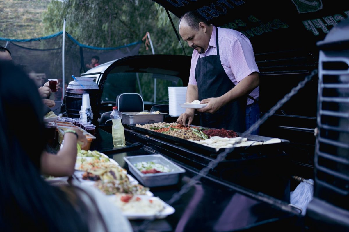 A Mr. Tako cook plating fajita, chorizo and salsa from a large catering spread.